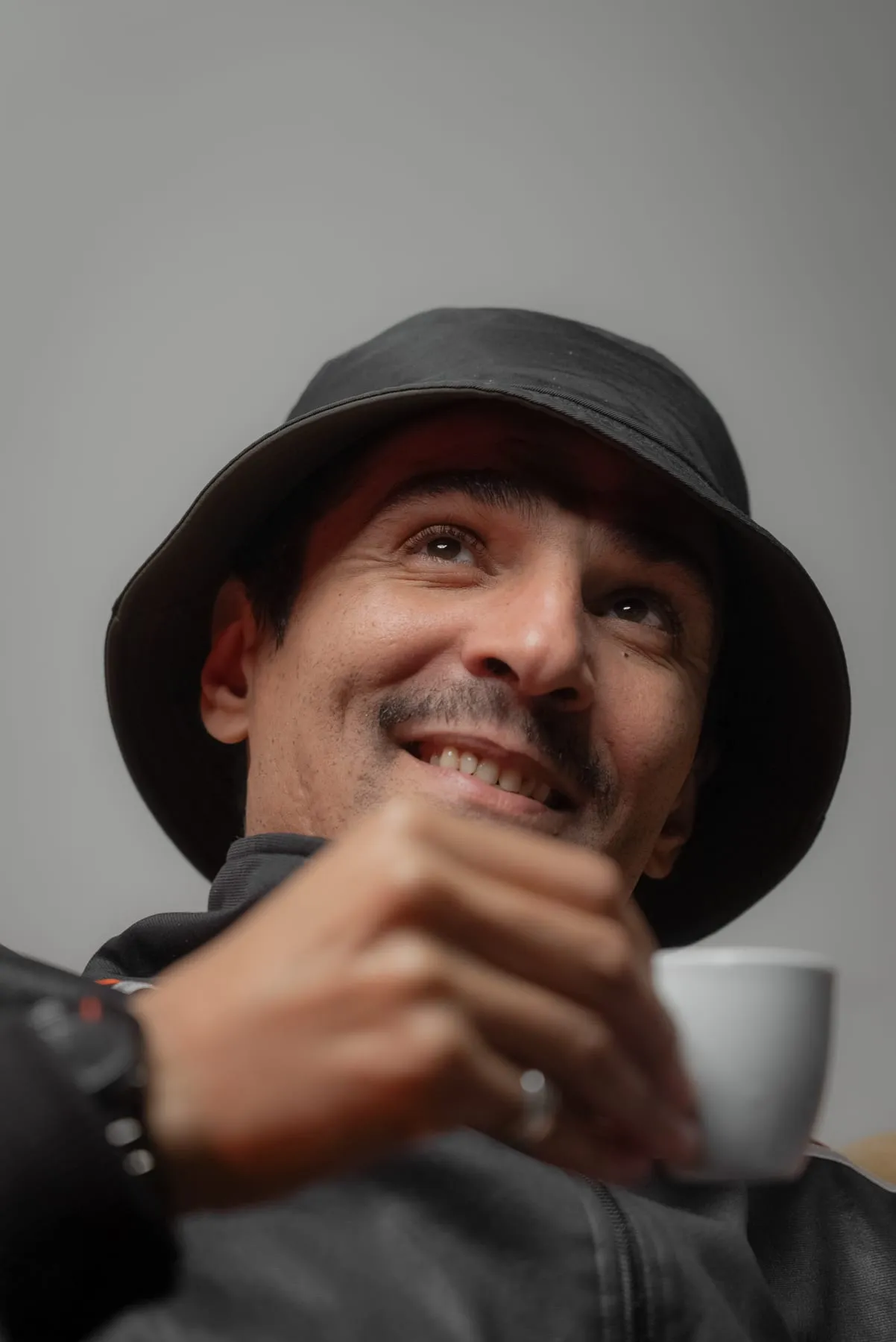 Zaamom smiling with a cup of coffee, wearing a bucket hat