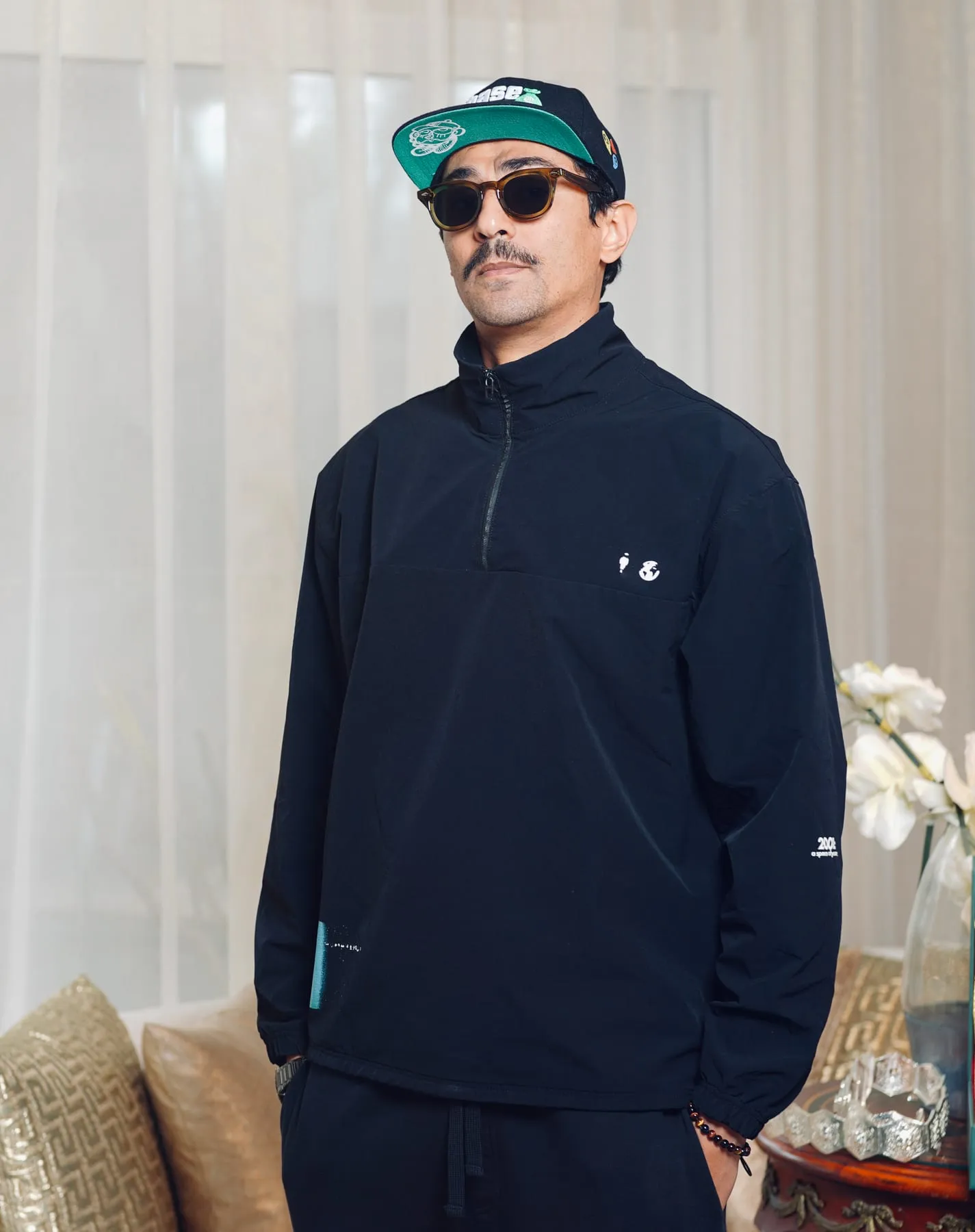 Zaamom standing, wearing a cap and sunglasses